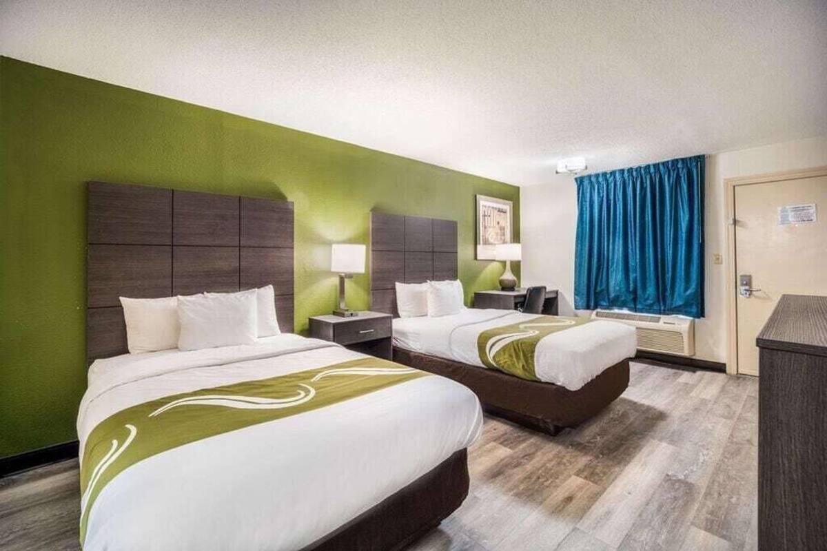 A hotel room with two beds, a green wall, a blue curtain, and a wooden floor.