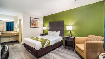 Una habitación de hotel con cama, una silla, un escritorio con espejo y una pared de acento verde.