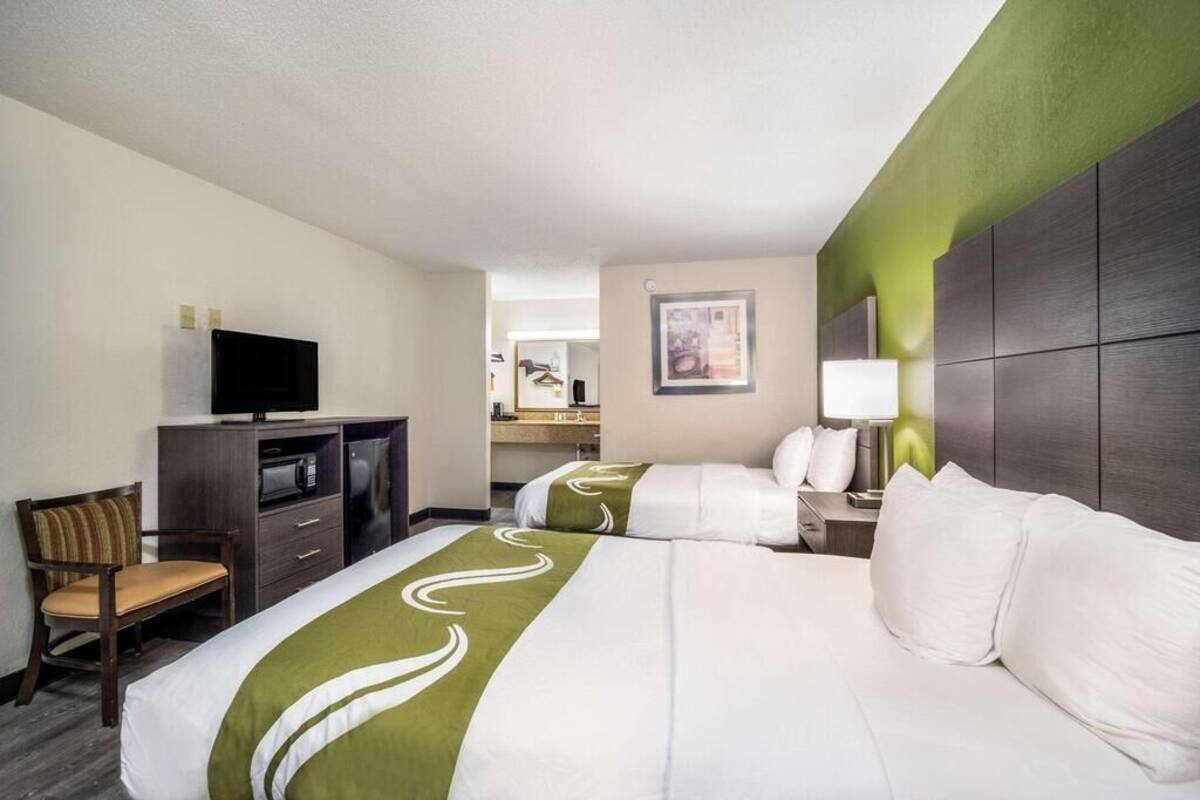 A hotel room with two beds, a desk with a television, a chair, and a mirror.