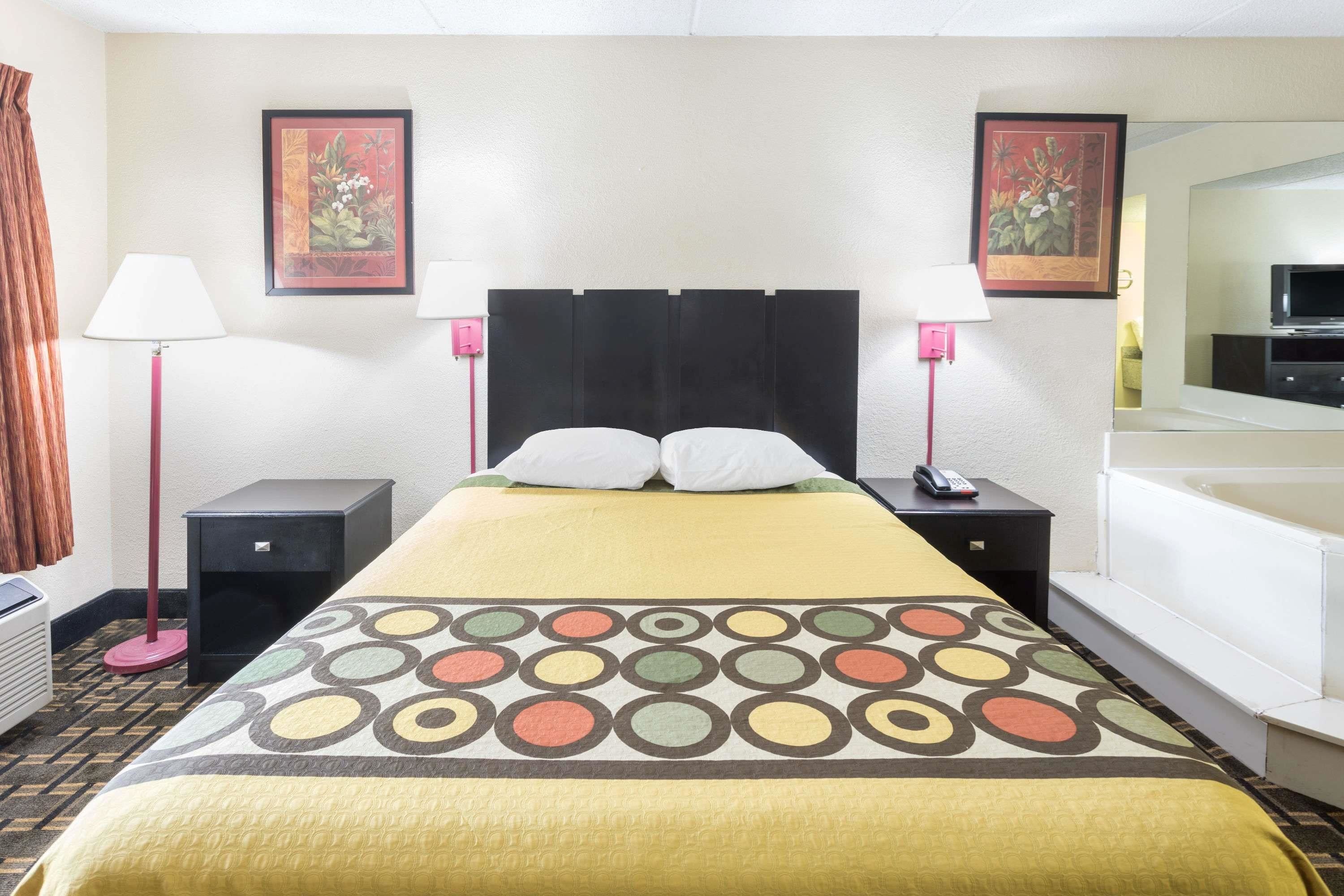 A hotel room with a bed, two bedside tables, a lamp, a TV, and a bathtub.