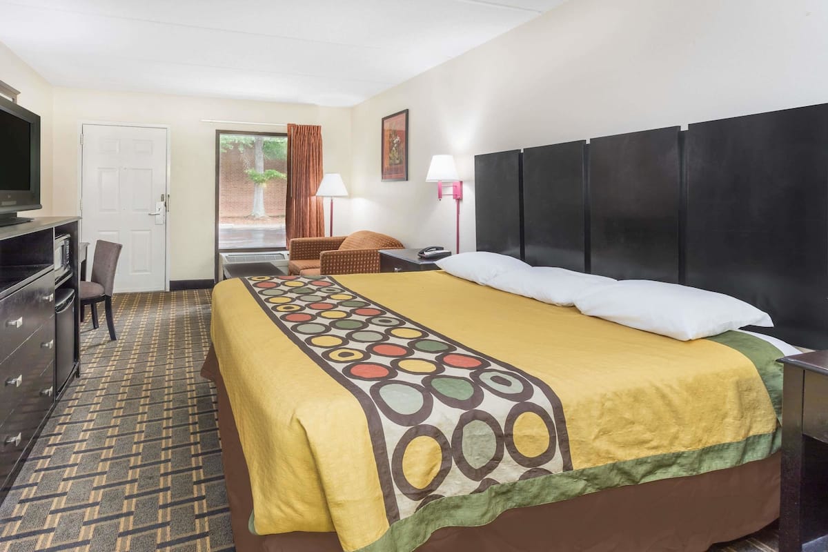 A hotel room with a bed, a desk, a chair, a TV, and a lamp.