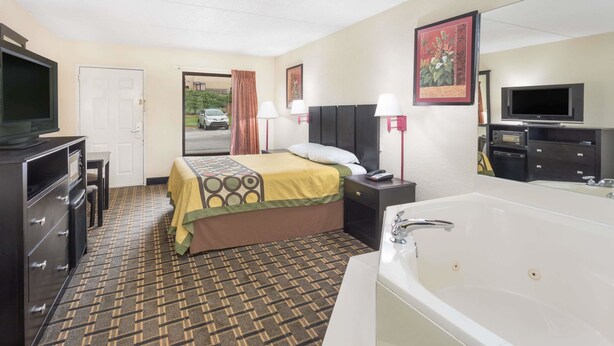 A hotel room with a bed, a TV, a desk, a lamp, a bathroom with a bathtub, and a door leading outside. - Super 8 by Wyndham Decatur/Lithonia/Atl Area (Decatur)