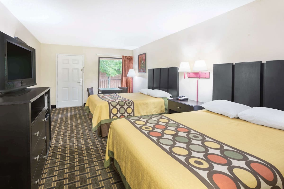 A hotel room with two beds, a TV, a desk, and a window with curtains.
