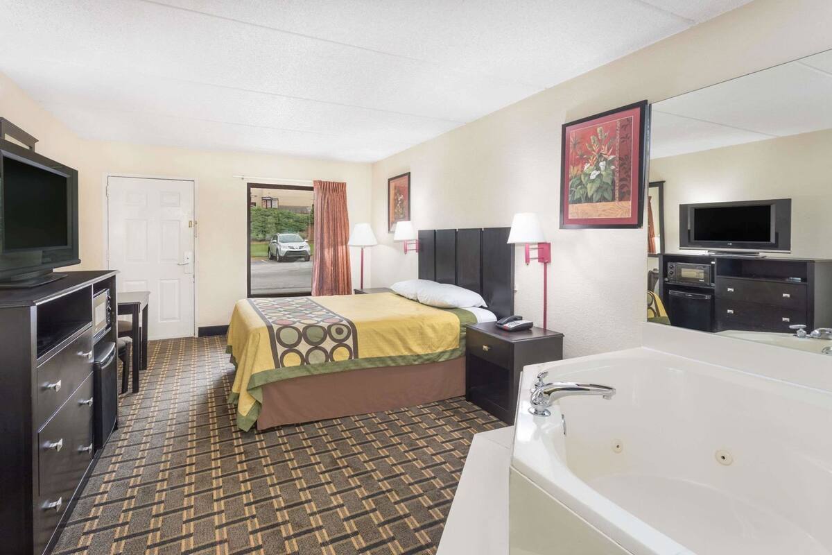 A hotel room with a bed, a desk, a TV, a bathroom with a bathtub, and a door leading to a parking area.