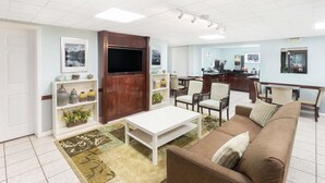 A living room with a brown sofa, white coffee table, and a TV. There are chairs, a kitchen area, and a dining table in the background. - Super 8 by Wyndham Decatur/Lithonia/Atl Area (Decatur)