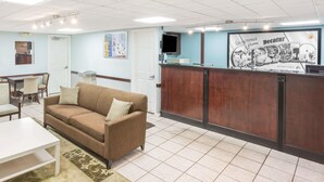 A reception area with a brown sofa, a white table, and a reception desk with a monitor. - Super 8 by Wyndham Decatur/Lithonia/Atl Area (Decatur)