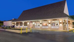 A building with a sloped roof, a lobby area, and a parking lot with yellow bollards. - Knights Inn Lebanon (Lebanon)