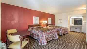 A hotel room with two beds, a desk, a chair, a desk lamp, a mirror, and a bathroom with a sink and towel rack.