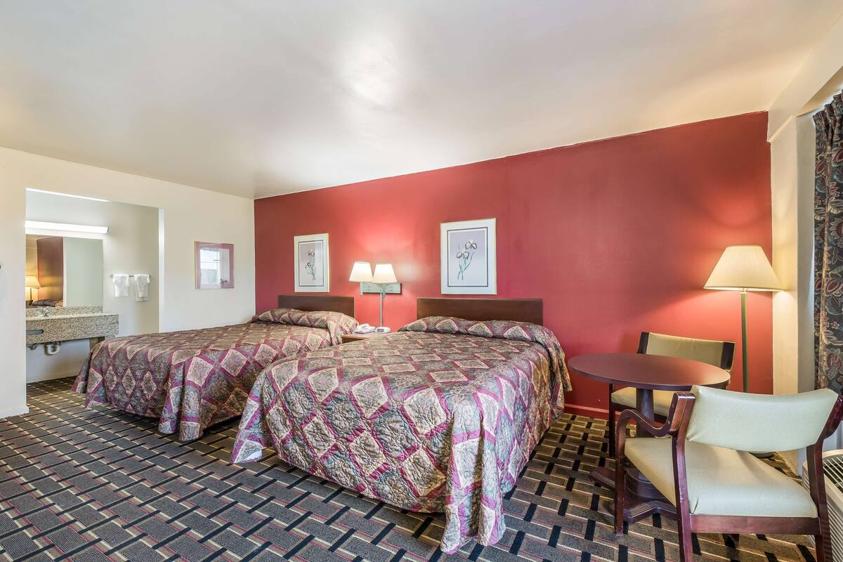 Habitación de hotel con dos camas, una mesita, una silla, una lámpara y un espejo.