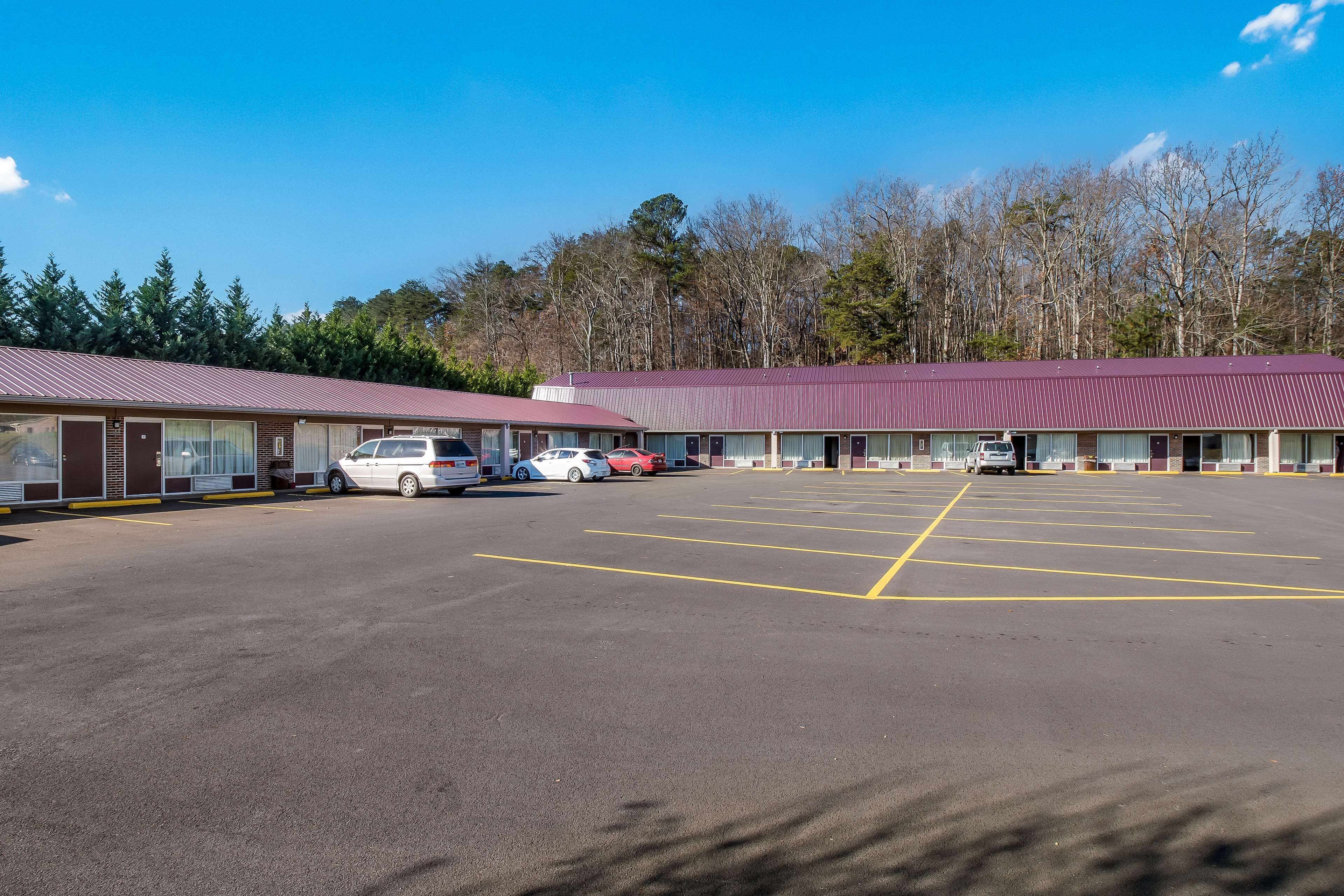 A parking lot with several cars, a building with a red roof, and trees in the background.