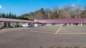 A parking lot with several cars, a building with a red roof, and trees in the background.