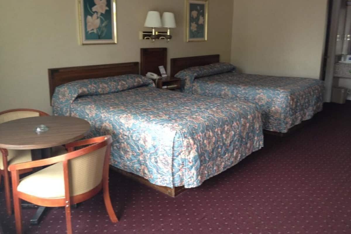Habitación de hotel con dos camas, una mesita pequeña, una silla y dos lámparas fijadas a la pared.