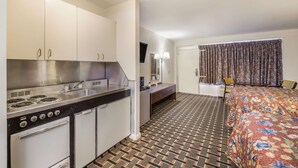 A compact hotel room with a kitchenette, a bed with floral bedding, a patterned floor, and a curtain with a paisley design. - Knights Inn Cleveland, TN (Cleveland)