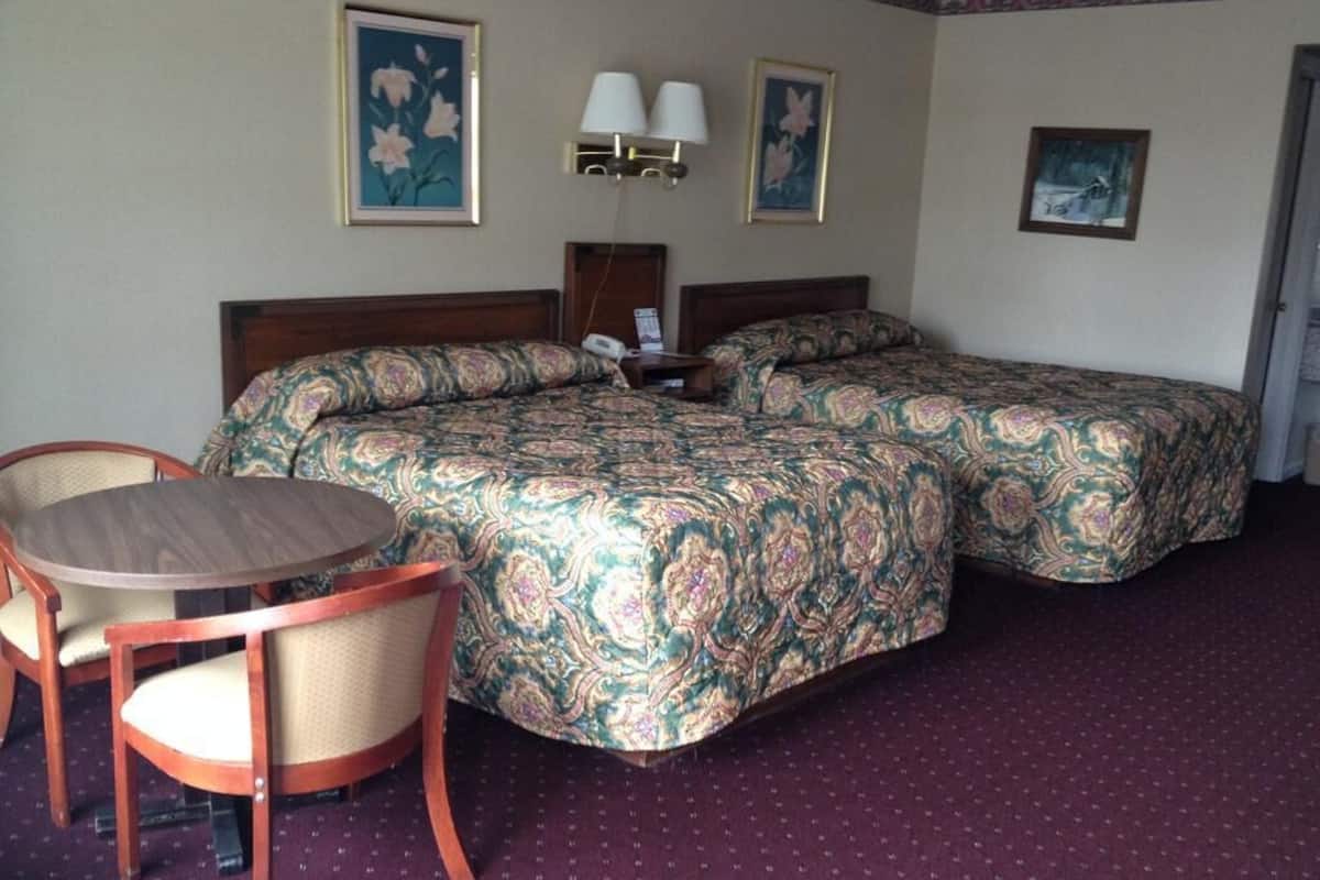 Habitación de hotel con dos camas, una mesa redonda de madera y dos sillas.