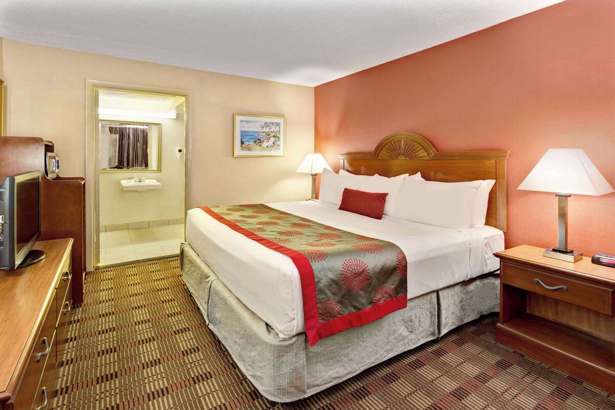 A hotel room with a bed, bedside lamps, a television, a desk, and a bathroom door.