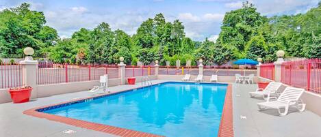 A rectangular pool with a red border, surrounded by white lounge chairs and a red fence.
