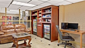 A room with a leather couch, a glass-top coffee table, a wooden desk with a computer, and a vending machine. - Ramada by Wyndham Baltimore West (Catonsville)