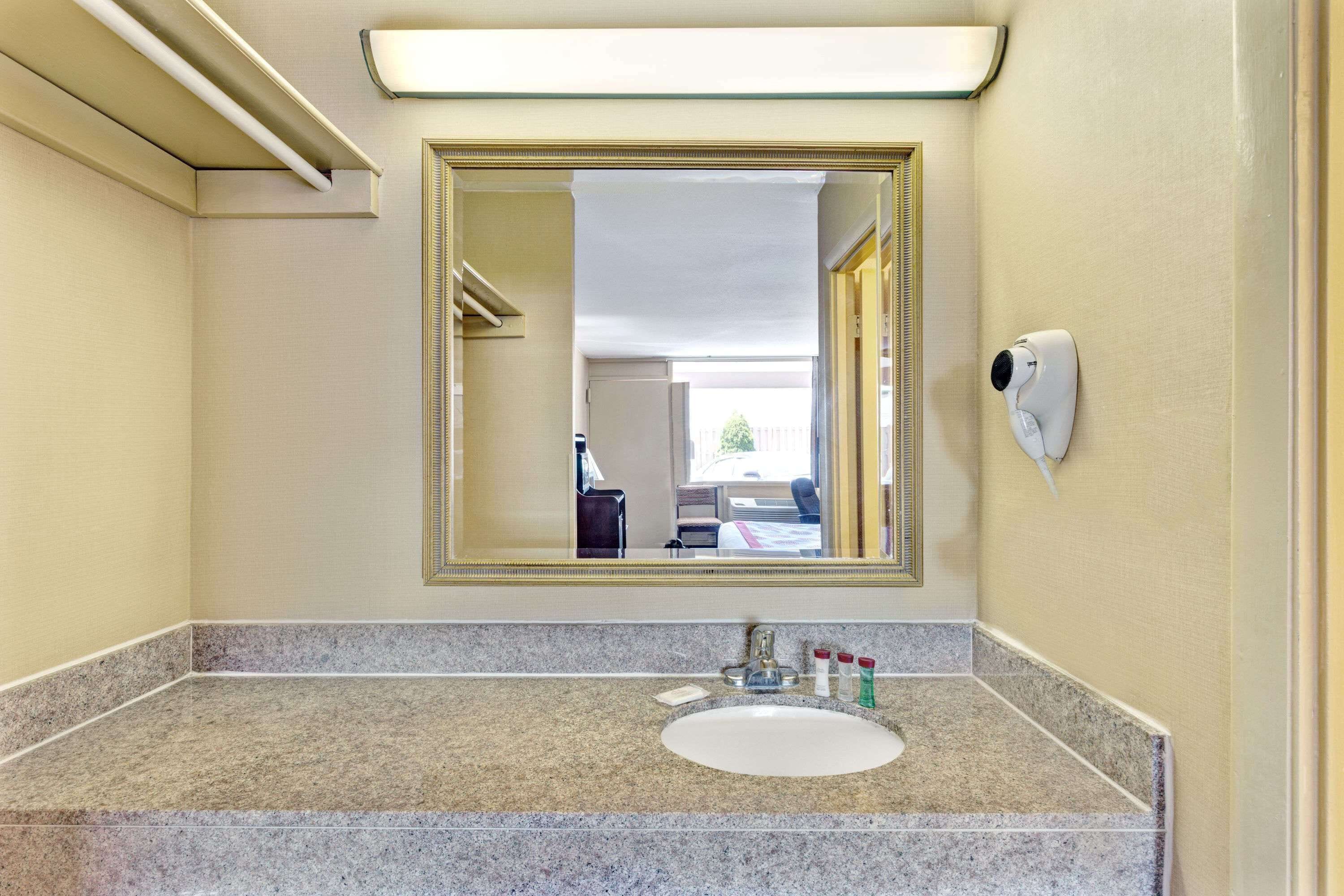Un baño con encimera de granito, lavabo, espejo y secador de manos.