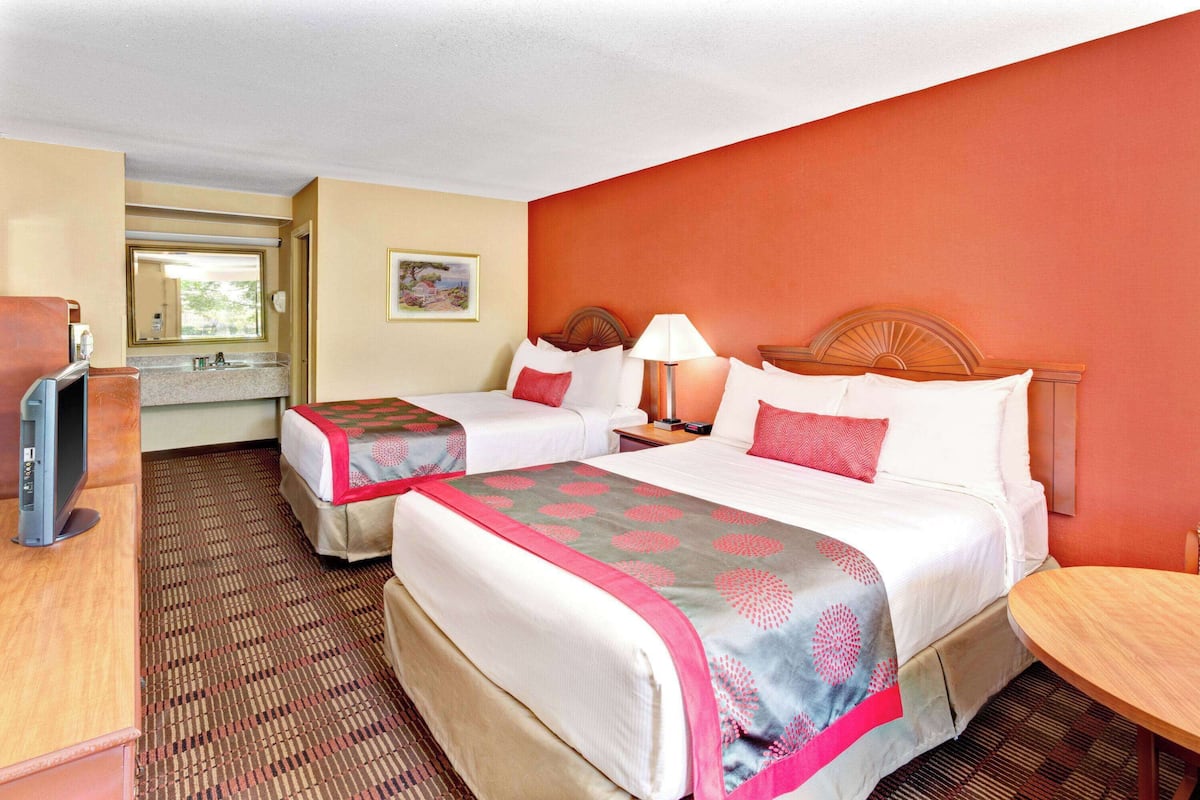 A hotel room with two beds, a desk, a television, and a bathroom visible through an open door.