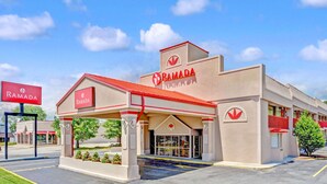 A Ramada hotel with a red and beige facade, a covered entrance, and a parking lot. - Ramada by Wyndham Baltimore West (Catonsville)