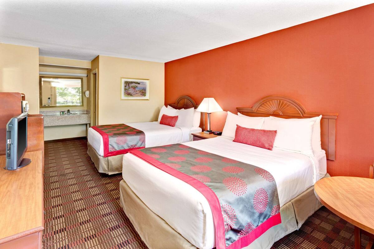 A hotel room with two beds, a desk, a television, and a bathroom visible through an open door.