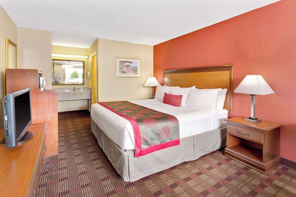A hotel room with a bed, bedside tables, a TV, a bathroom, and a window.