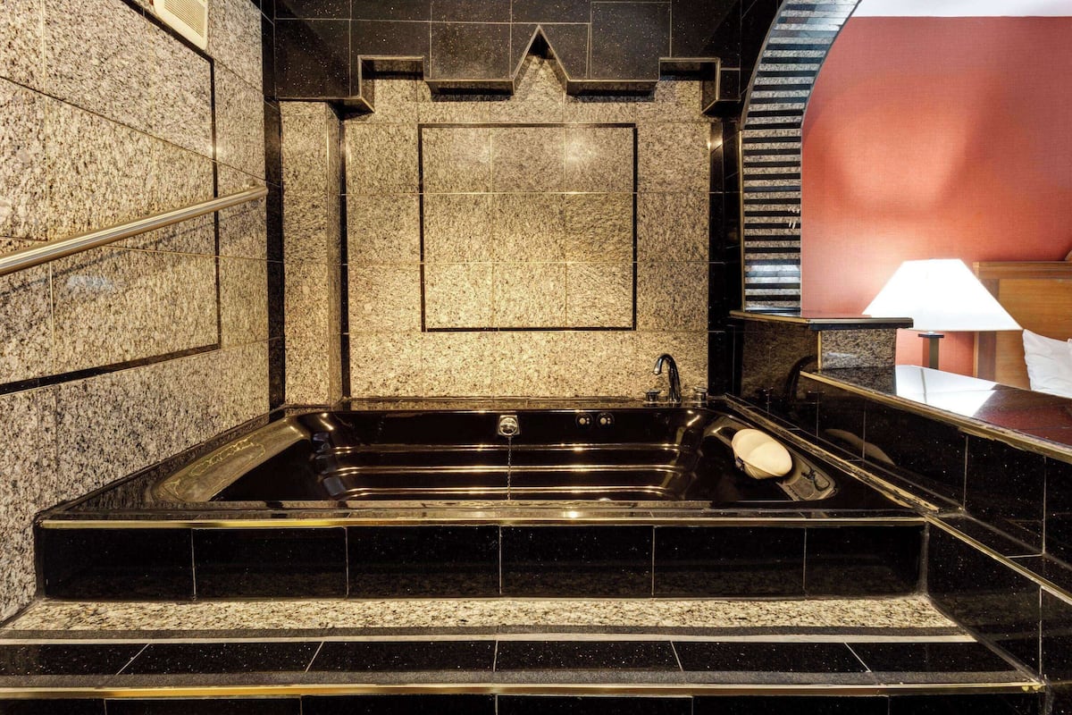 A black marble bathtub with a wooden bench, a handrail, and a red wall in the background.
