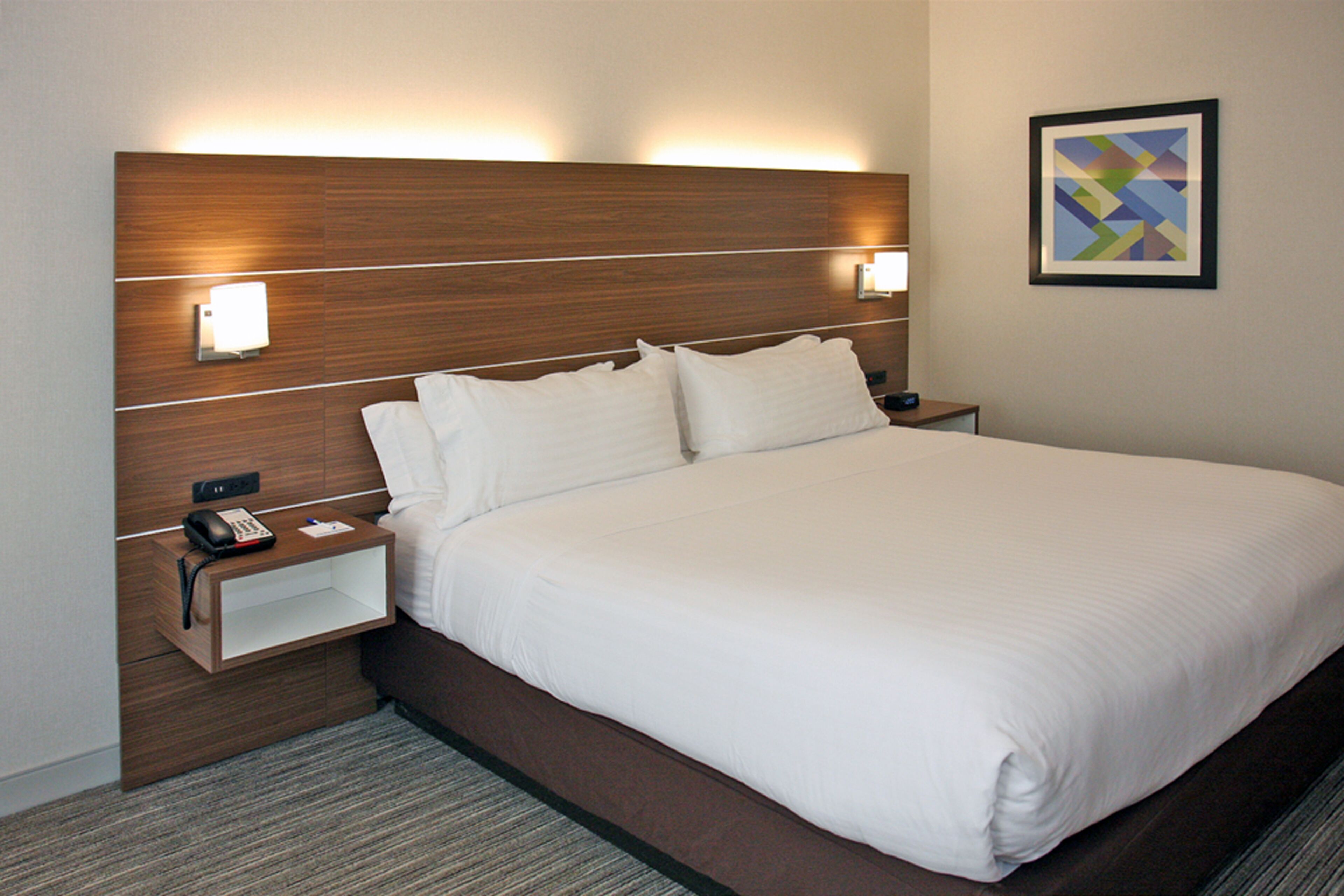 A hotel room with a large bed, bedside tables, a telephone, and a framed picture on the wall.