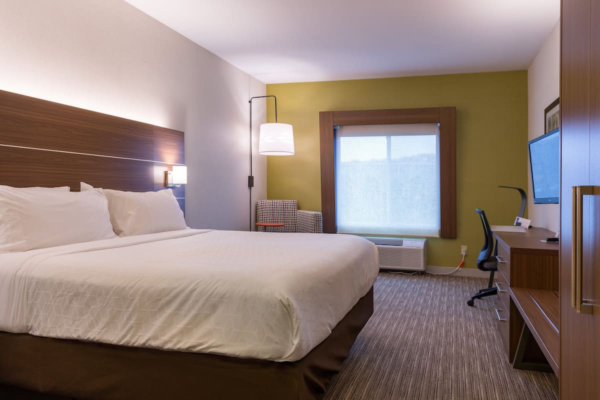 A hotel room with a large bed, a desk, a chair, a window, and a television.