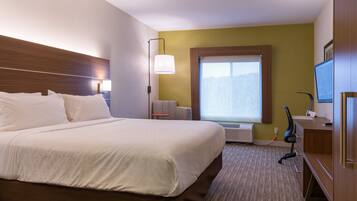 A hotel room with a large bed, a desk, a chair, a window, and a television.