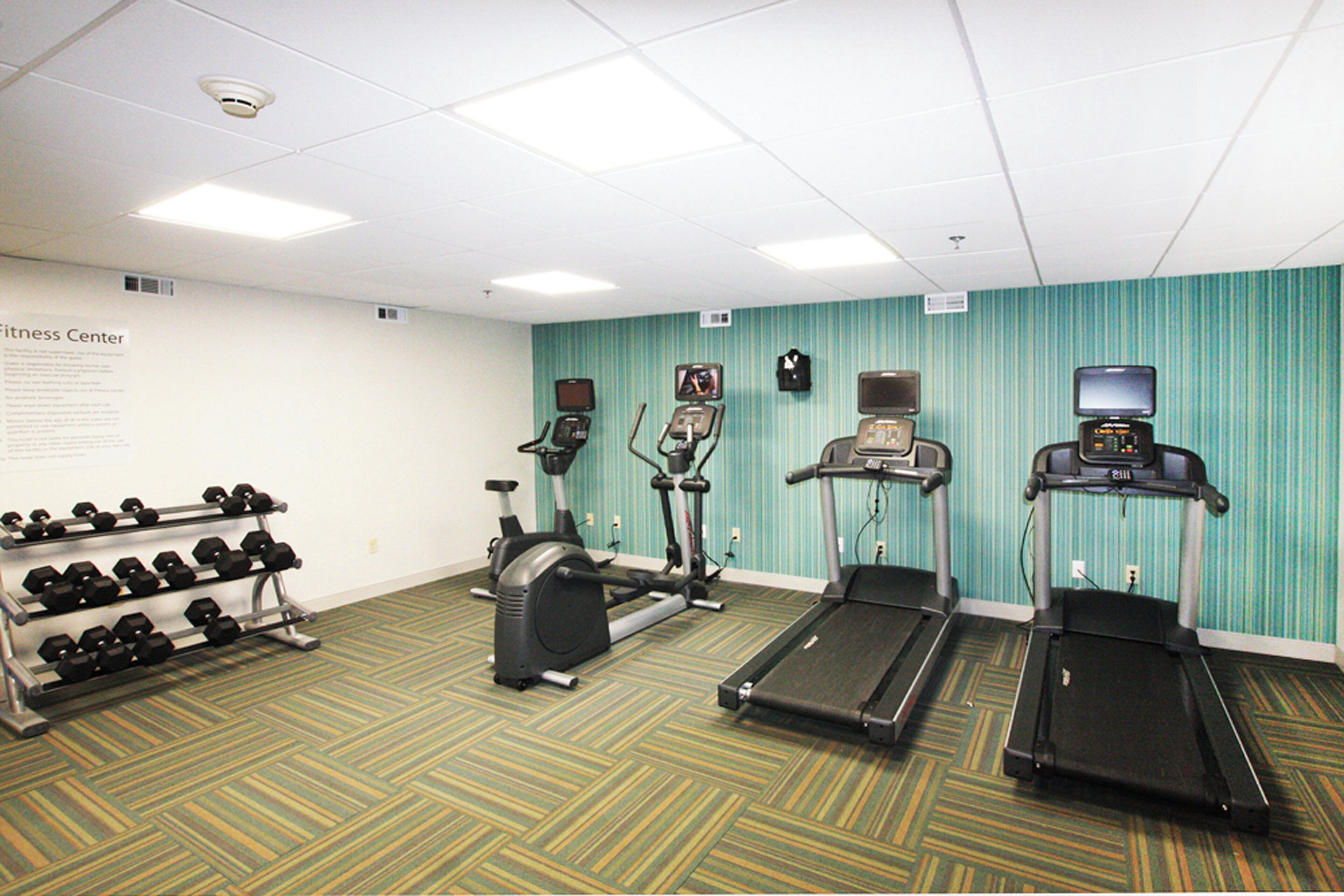 A fitness center with treadmills, an elliptical, and a dumbbell rack.
