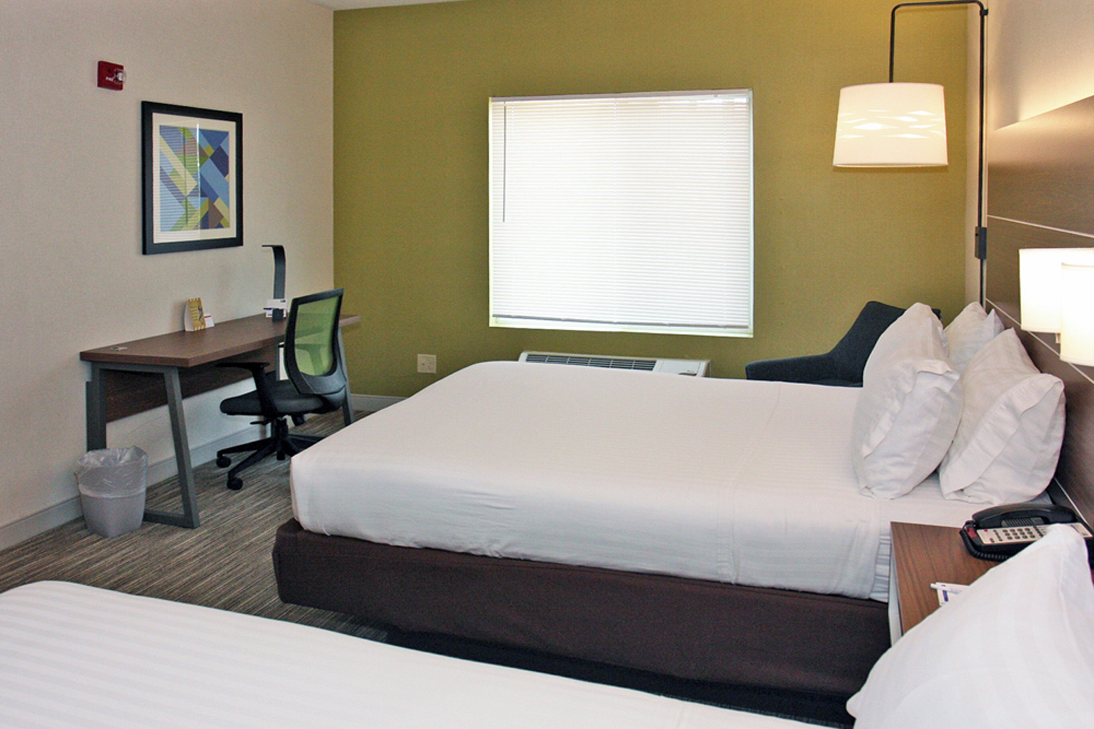 Habitación de hotel con cama, escritorio, silla, lámpara y ventana.