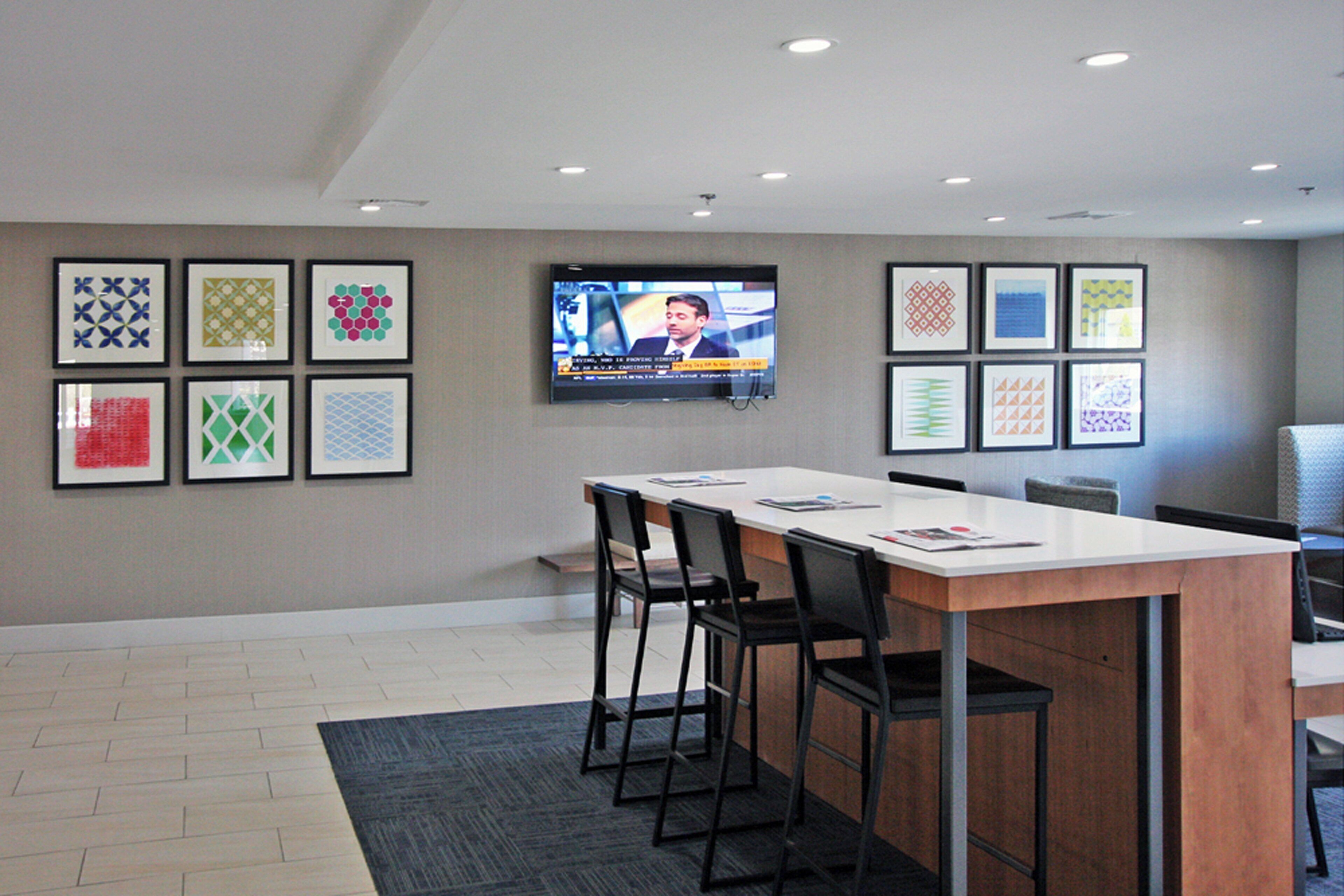 A conference room with a long table, chairs, a flat-screen TV mounted on the wall, and framed geometric patterns on the walls.