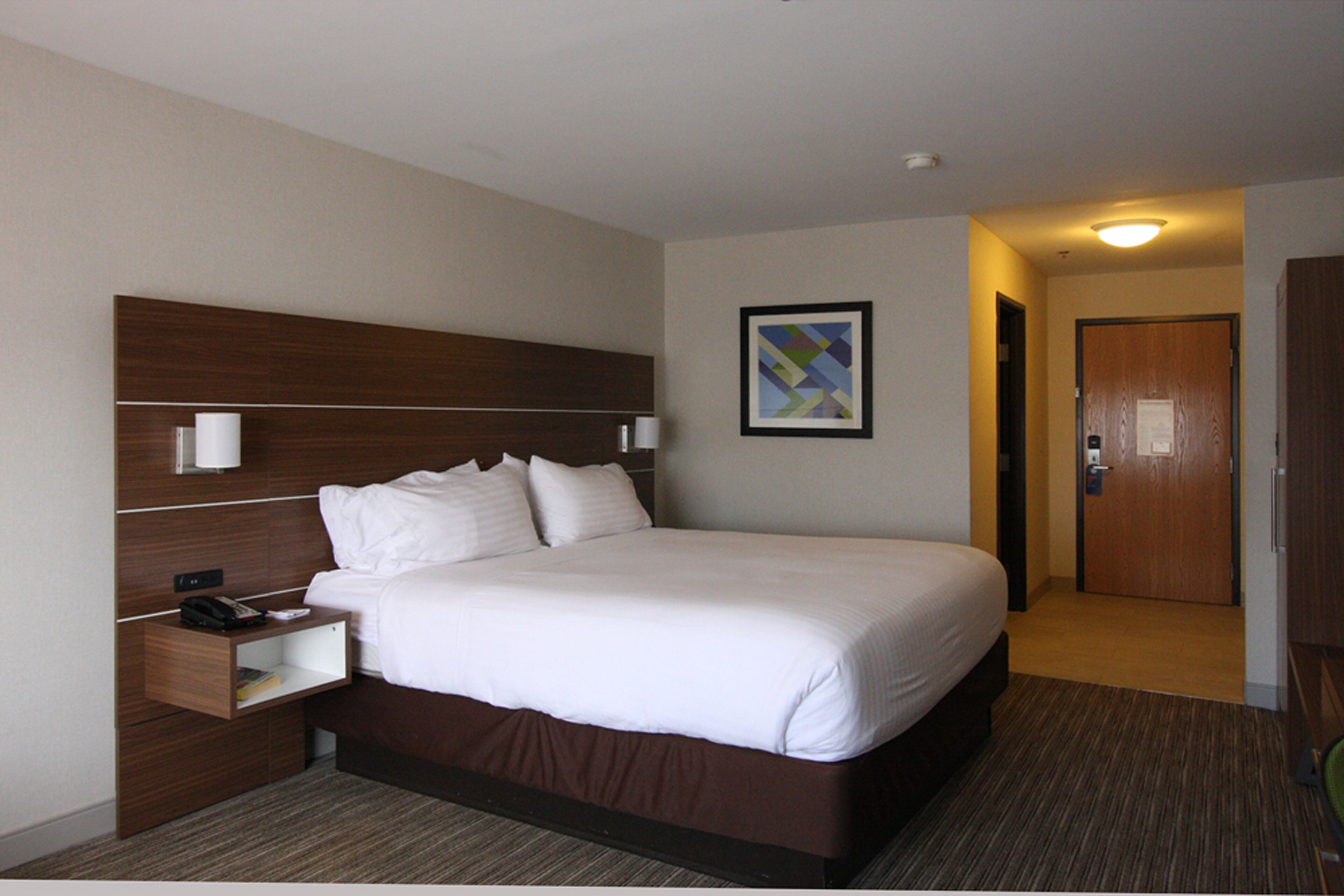 A hotel room with a large bed, a bedside table with a lamp, and a framed picture on the wall.