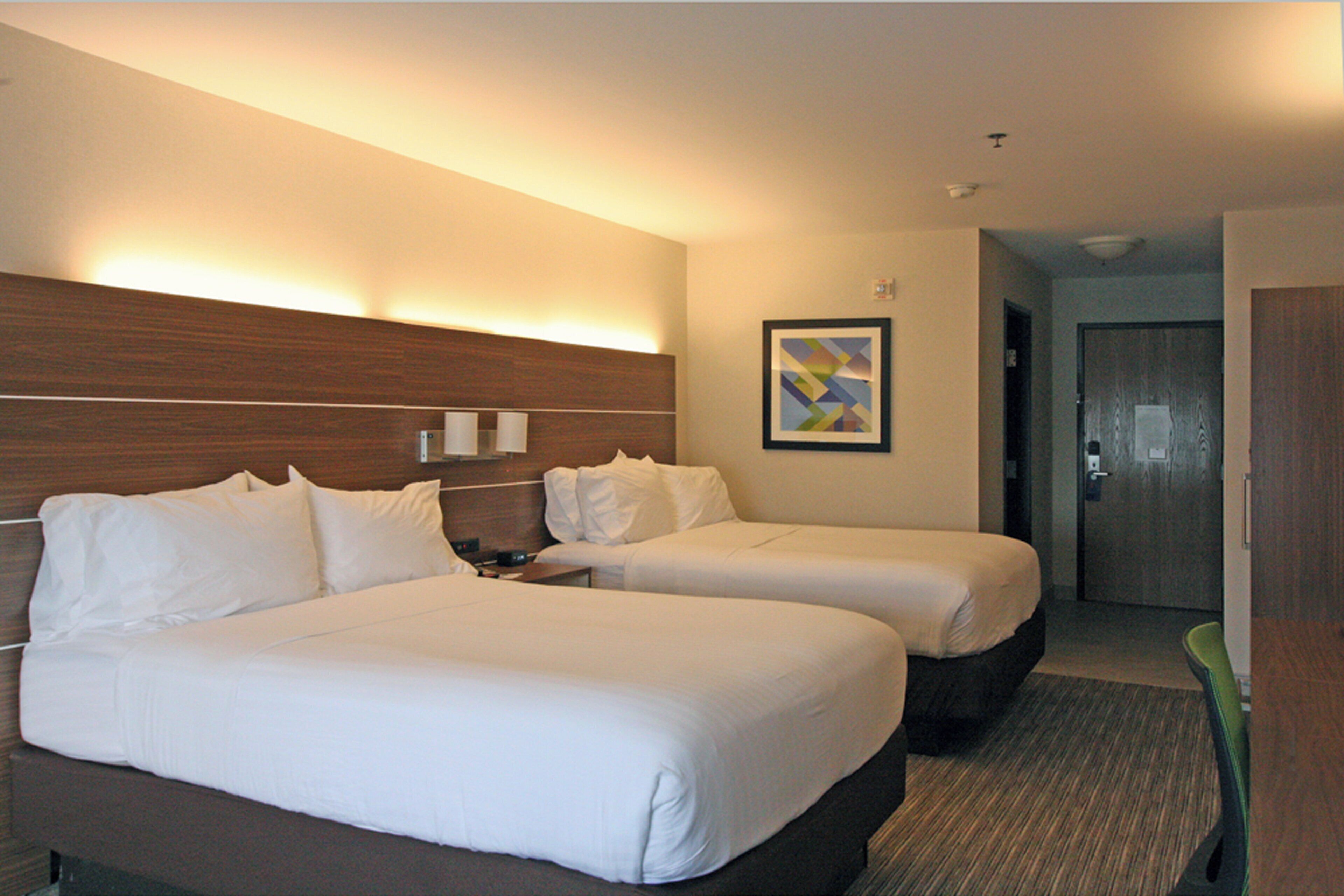 A hotel room with two beds, a nightstand, a wall-mounted lamp, and a framed picture.