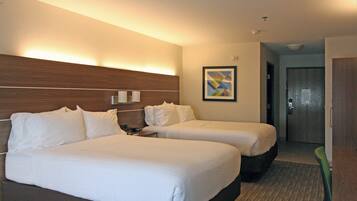 A hotel room with two beds, a nightstand, a wall-mounted lamp, and a framed picture.