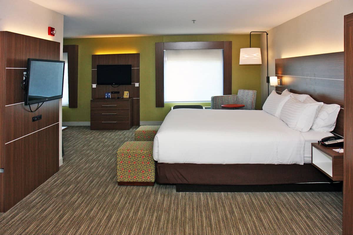 A hotel room with a large bed, a TV, a desk with a lamp, a chair, and a small table.