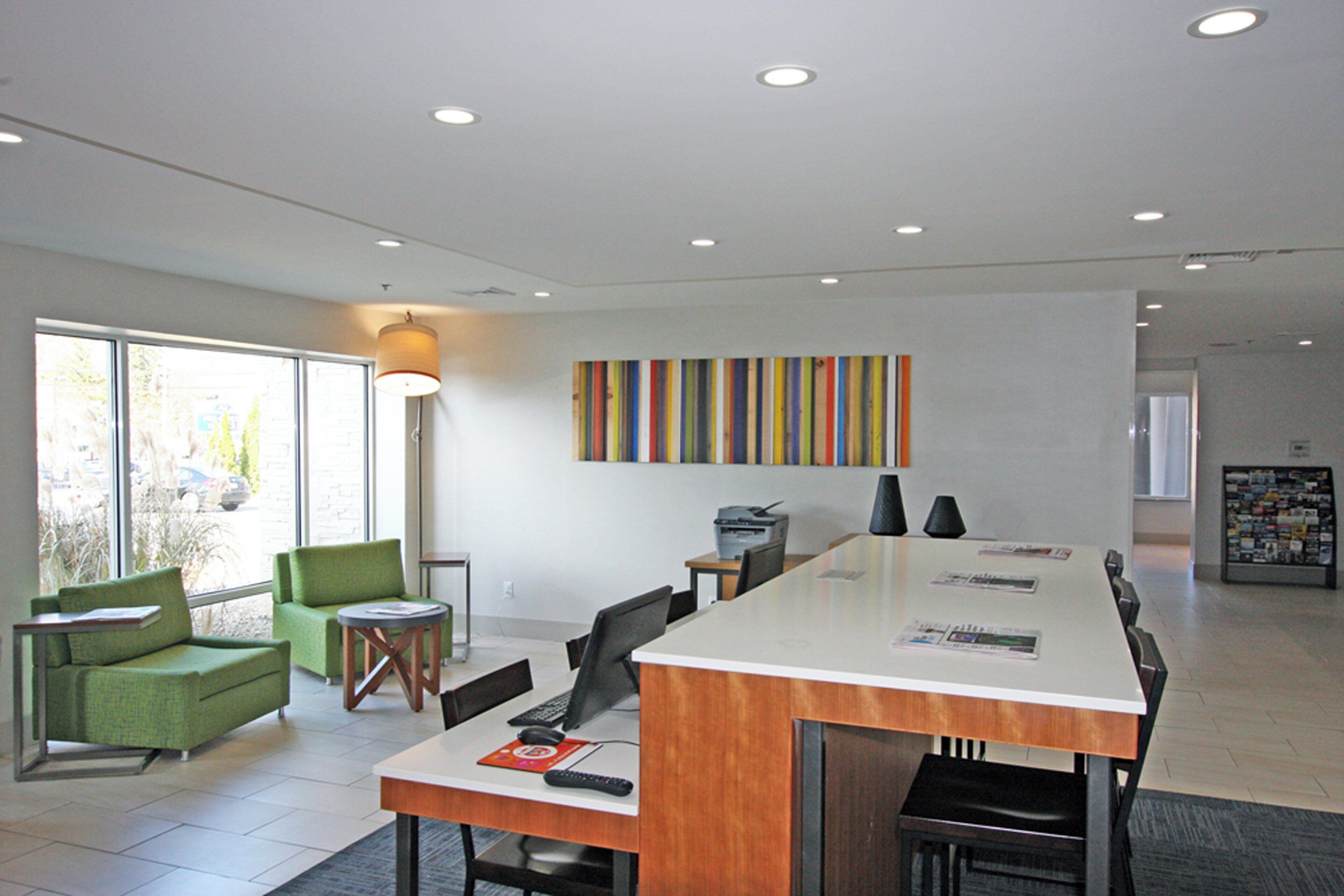 A modern office space with a long table, chairs, a printer, and a colorful abstract painting on the wall.