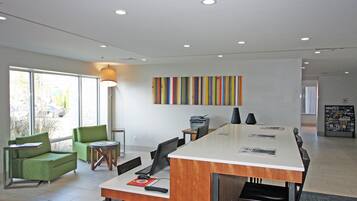 A modern office space with a long table, chairs, a printer, and a colorful abstract painting on the wall.