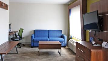 Una habitación de hotel con un sofá azul, un escritorio de madera, una computadora, un televisor y un mueble bajo.
