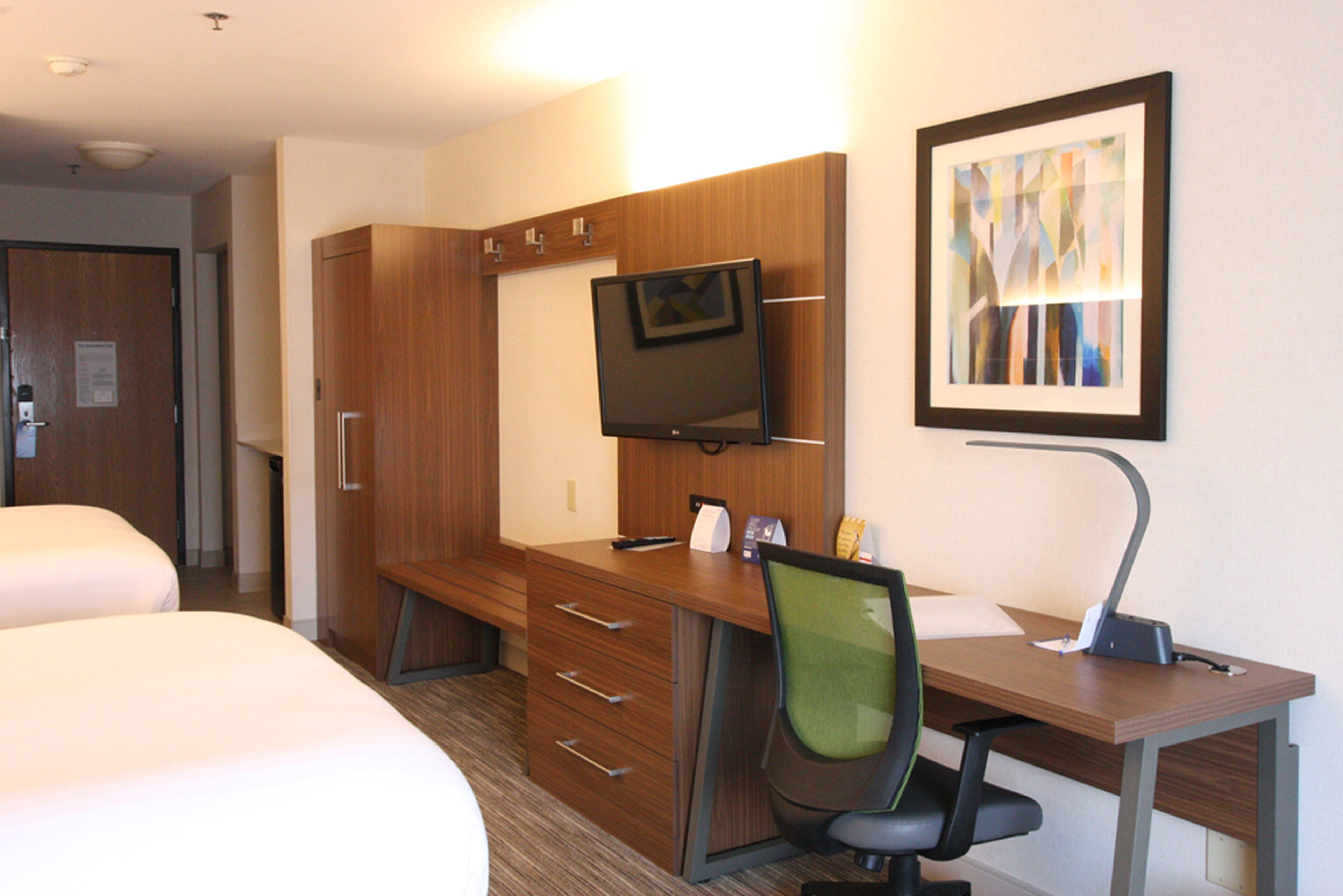 Habitación de hotel con dos camas, un escritorio con silla, televisor y un cuadro en la pared.