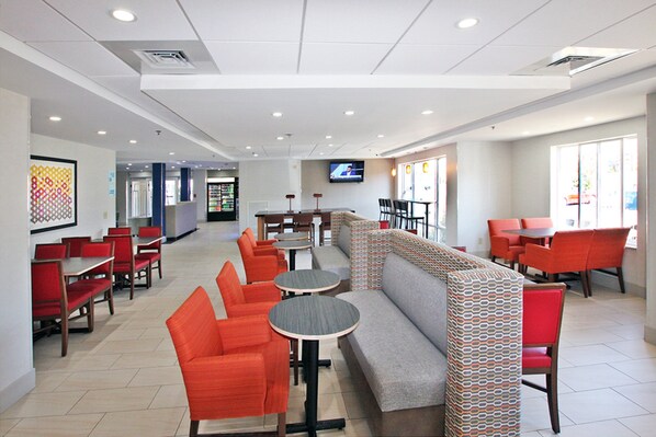 A modern restaurant with red and grey seating, a TV screen, and a patterned wall. - Holiday Inn Express Branford-New Haven by IHG (Branford)