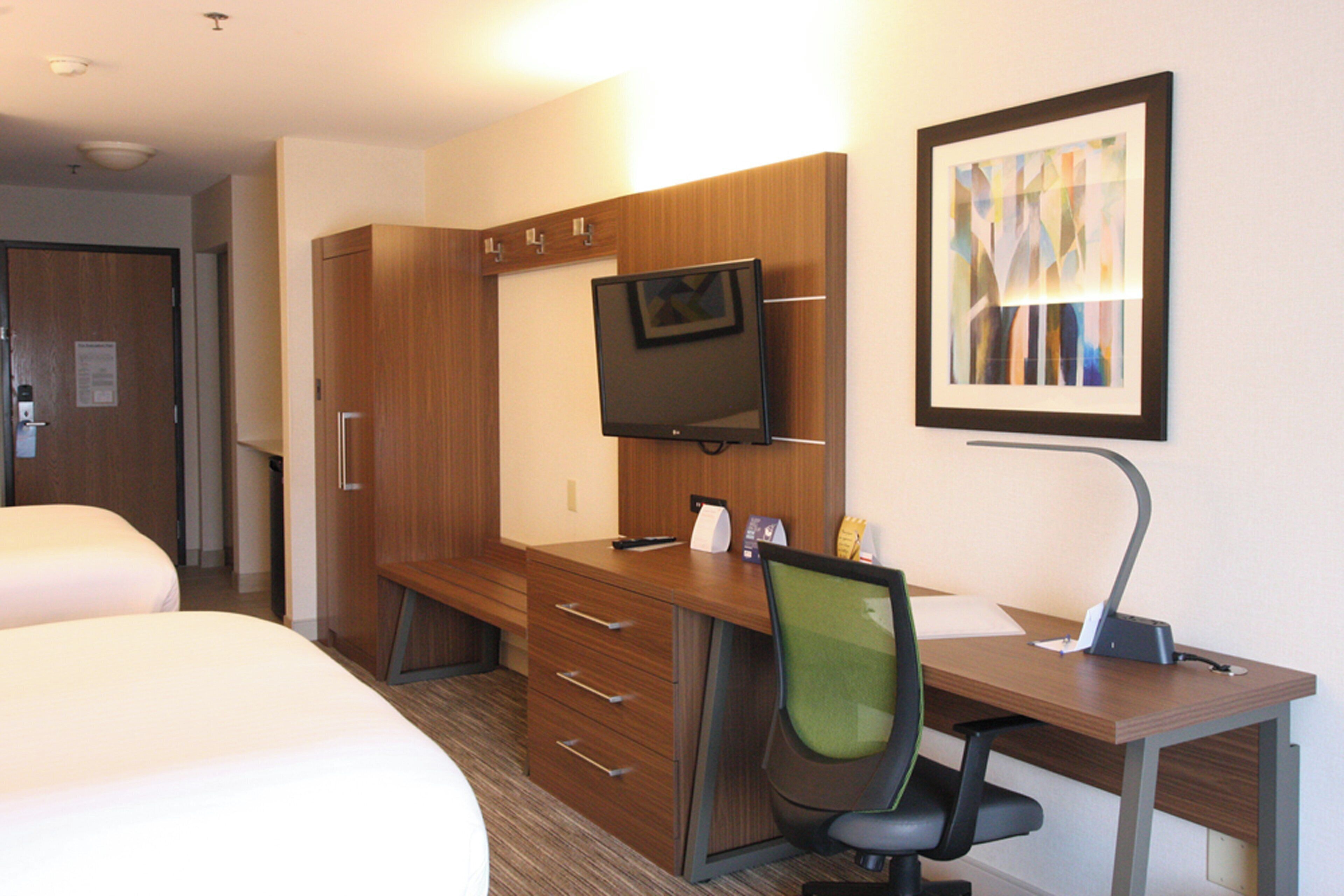 A hotel room with a bed, a desk with a chair, a television, and a framed picture on the wall.