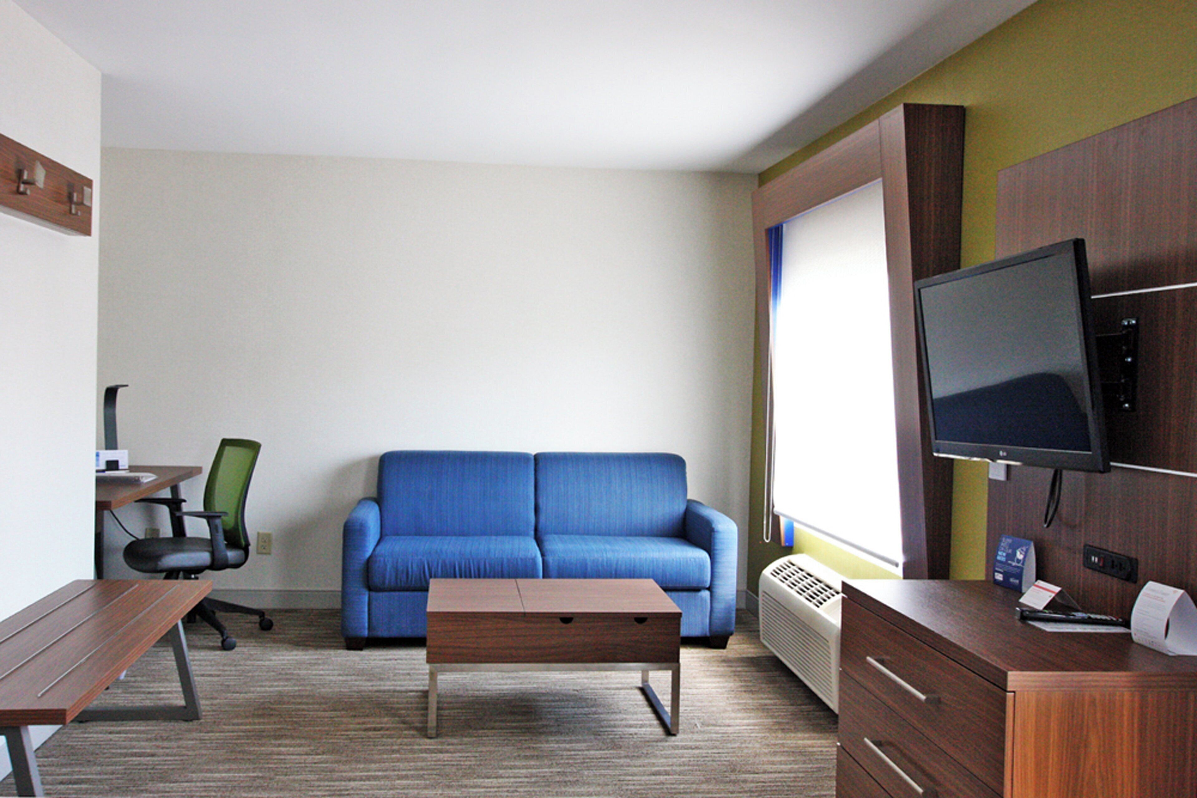 A hotel room with a blue sofa, a wooden desk, a chair, a television, and a radiator.