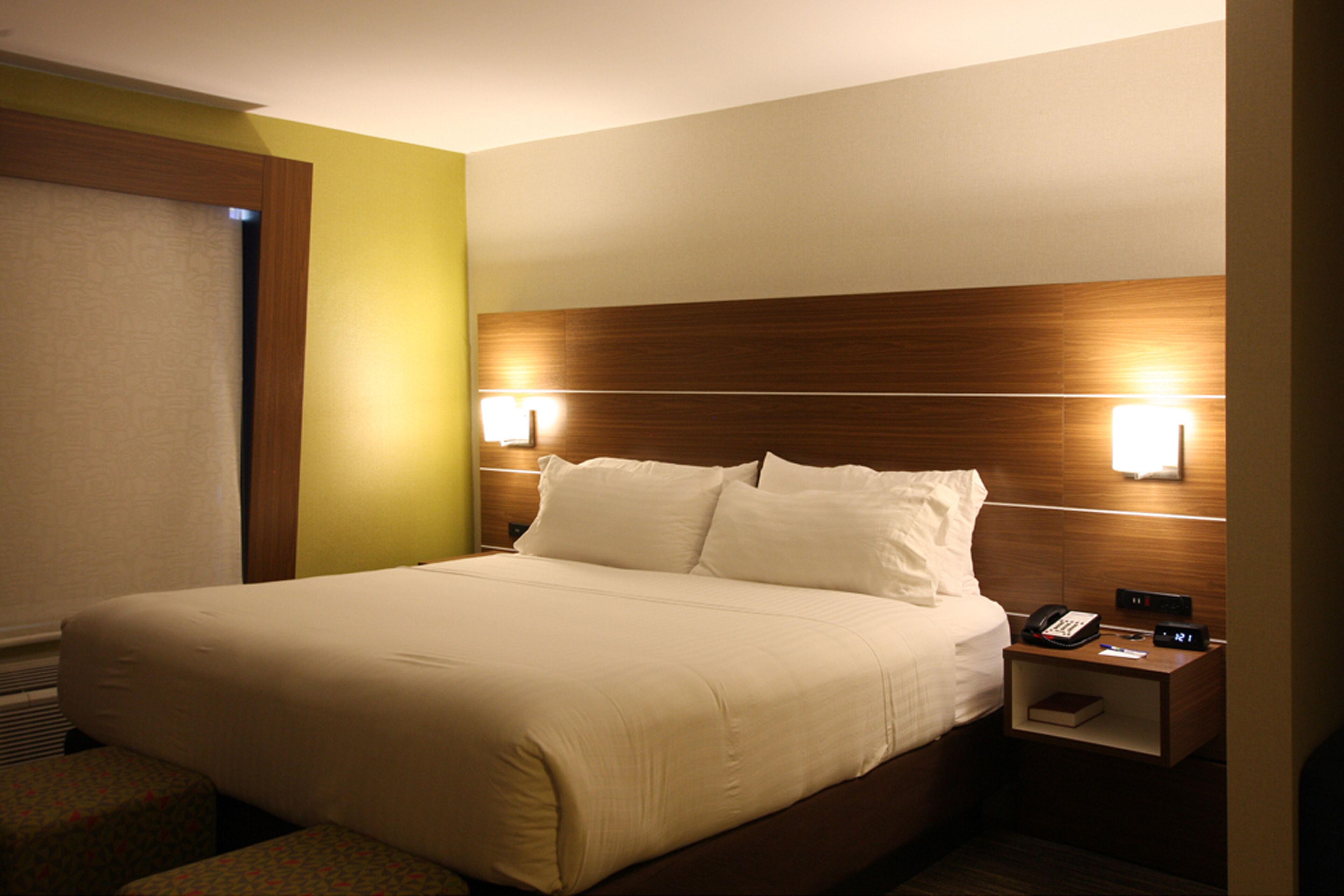 A hotel room with a large bed, two bedside tables, and a nightstand with a phone and a lamp.