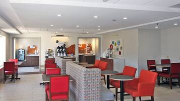 Een modern restaurant met rode stoelen en tafels, een balie met een koffieapparaat en een muur met kleurrijke borden.
