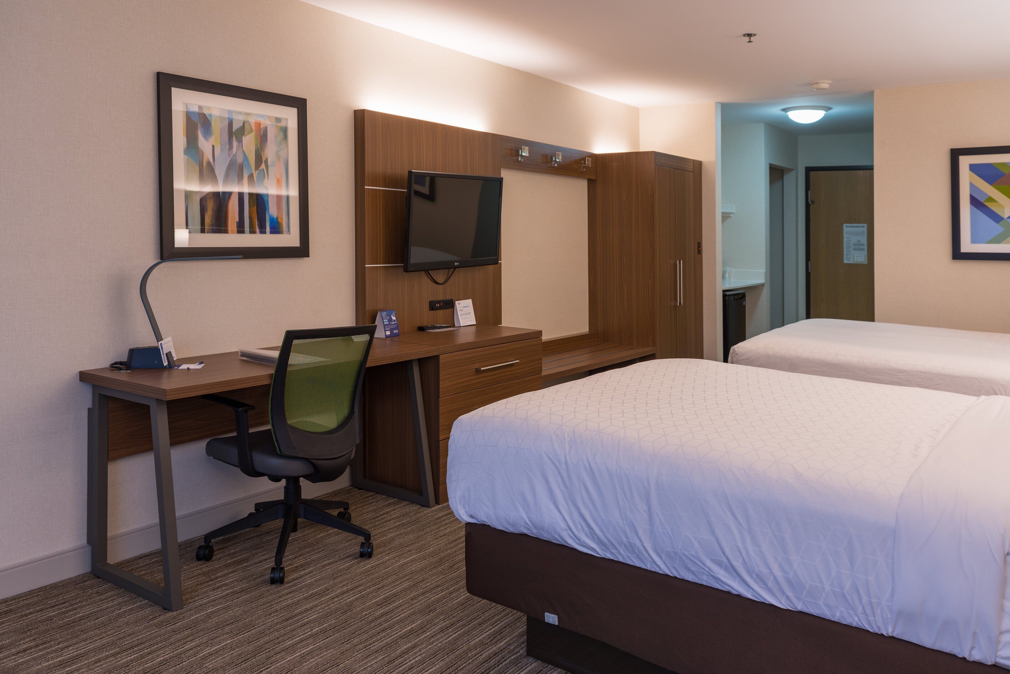 A hotel room with a desk, chair, television, wardrobe, and two beds.