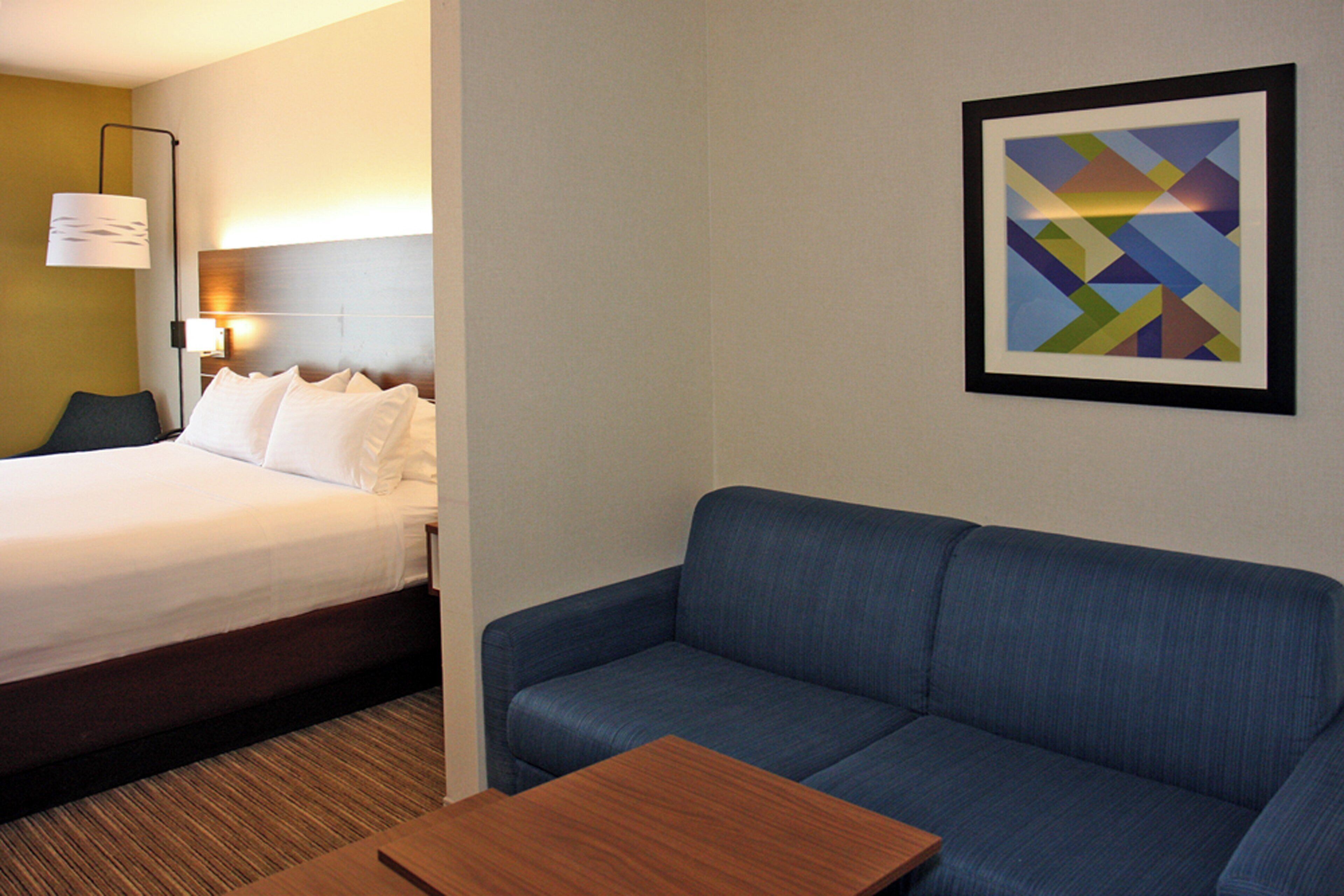 Un cuarto de hotel con una cama, un sofá azul, una mesita de madera y un cuadro abstracto enmarcado en la pared.