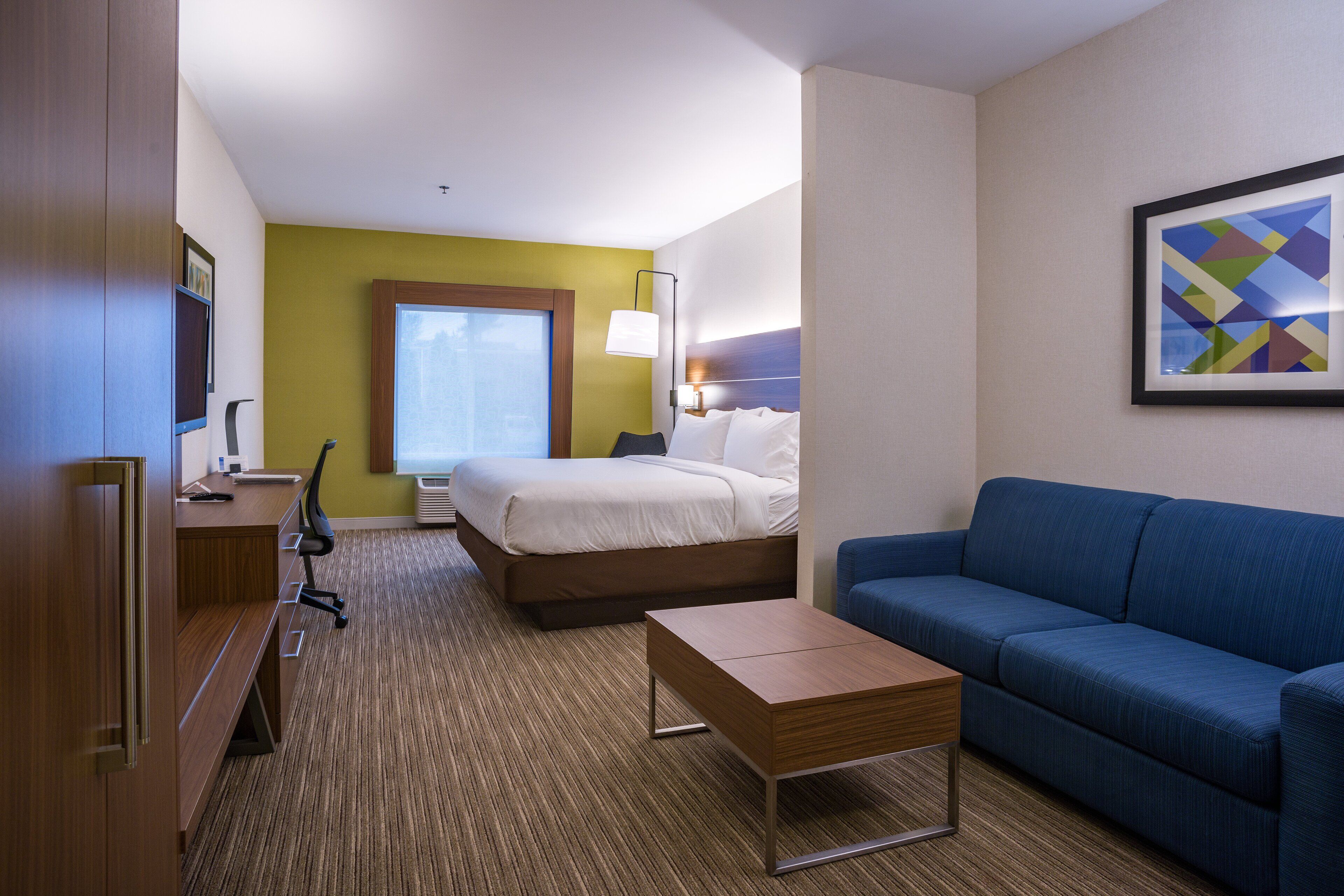 A hotel room with a bed, a blue sofa, a wooden desk, and a lamp.