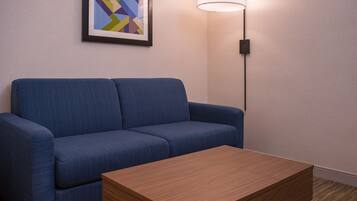 Un sofá azul y una mesa de centro de madera en una habitación con un cuadro abstracto enmarcado en la pared y una lámpara de pie.